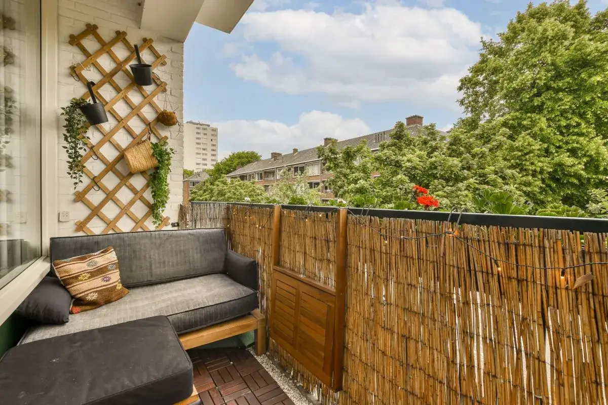 Jak osłonić balkon w bloku? Uroczy kącik z sofą i bambusową osłoną, idealny na relaks.